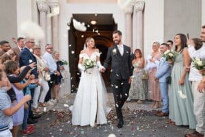 Mariage : sortie d'église des mariés sous une pluie de pétales. Photo de mariage joyeuse et festive.