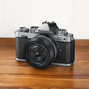 Appareil photo Nikon Z fc argenté avec objectif Nikkor Z 28mm sur table en bois.