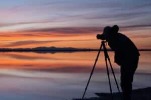 Photographe avec trépied devant un coucher de soleil. Choisir son trépied photo reflex, hybride, Canon, Nikon, Sony, Fujifilm, Panasonic.
