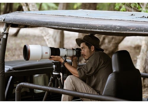 Photographe animalier avec Sony A1 II et téléobjectif sur un safari en jeep pour capturer la faune.