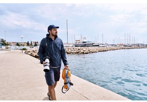 Photographe Sony A1 II au bord de l'eau avec un téléobjectif, marina en arrière-plan. Paysage marin.