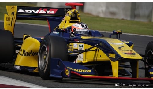 Voiture de course jaune et bleu sur piste, photographiée avec Sony RX10 IV. 