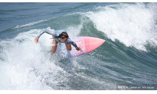 Surfeuse sur une vague avec Sony RX10 IV. Surf, eau, vague, planche de surf rose.