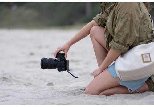 Sony A7 V sur la plage: femme prenant une photo avec un appareil photo Sony. Objectif et écran visibles.