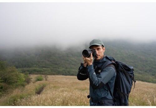 Photographe avec Sony A7 V en nature brumeuse. Sac à dos, paysage montagneux. Idéal pour photo de voyage et équipement Sony.
