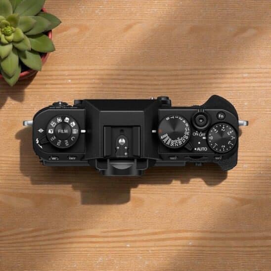 Fujifilm X-T30 III top view on wood. Black camera with dials for ISO, shutter speed, and exposure compensation settings. 