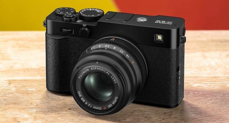 Fujifilm X-E5 noire de côté avec objectif Fujinon 35mm sur une table en bois, fond jaune et rouge.