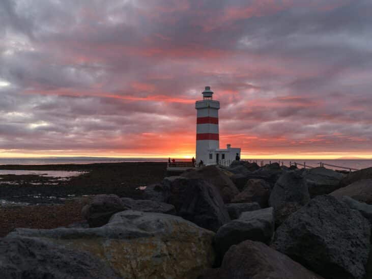 Phare rayé rouge et blanc au coucher du soleil en Islande. Rochers au premier plan. Photographie Hasselblad X2D II 100C.