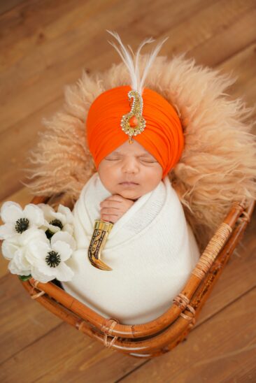 Nouveau-né emmailloté dans un panier, coiffé d'un turban orange orné. Photo de bébé artistique pour réussir vos clichés de nouveau-nés.