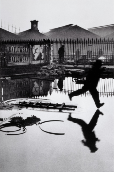 Photographie noir et blanc de Henri Cartier-Bresson, "Derrière la Gare Saint-Lazare", un homme sautant au-dessus d'une flaque.