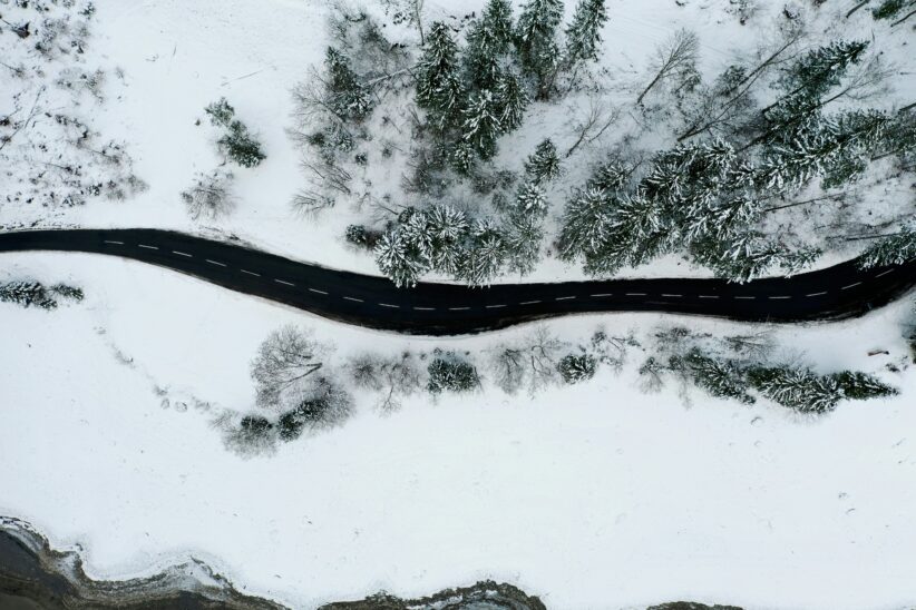 Photo aérienne d'une route sinueuse enneigée à ratio 2:3. Paysage hivernal avec des arbres couverts de neige.