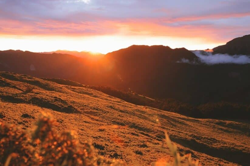 Soleil couchant derrière une crête de montagne, herbes dorées au premier plan