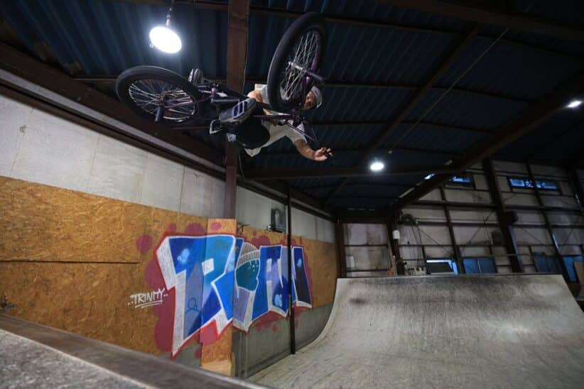 Cycliste BMX en plein saut au-dessus d'une rampe dans un skatepark couvert, graffiti coloré au mur
