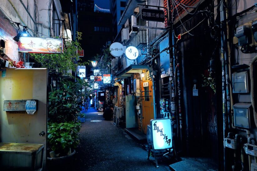 Ruelle étroite de nuit bordée d'enseignes lumineuses et de façades encombrées
