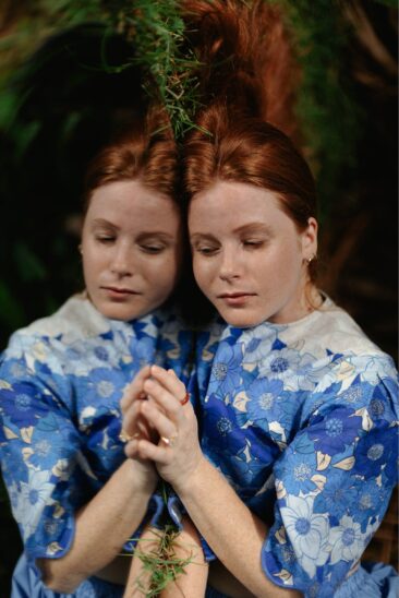 Portrait en double exposition d'une jeune femme rousse en robe bleue brodée, mains jointes