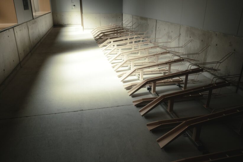 Couloir en béton traversé par une lumière rasante qui dessine les ombres de range-vélos