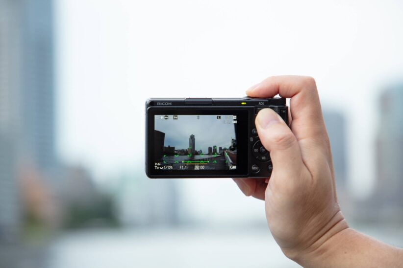 Photographe cadrant une vue urbaine sur l'écran arrière du Ricoh GR IV tenu d'une main