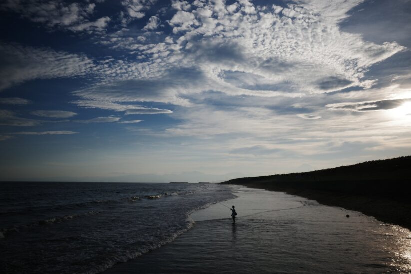 Plage en contre-jour sous un ciel nuageux, silhouette d'un baigneur dans les vagues
