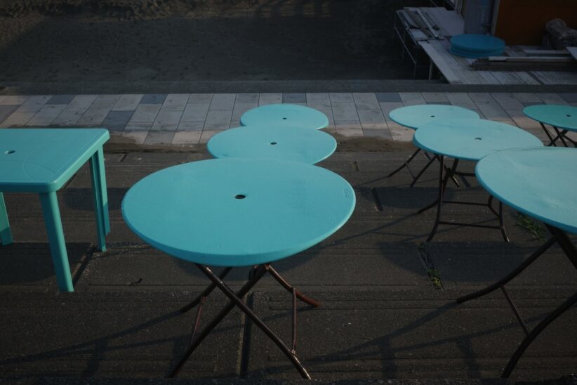 Tables rondes turquoise d'une terrasse vide sur un trottoir