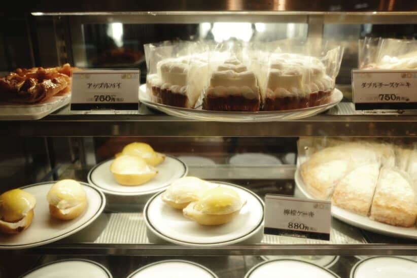 Vitrine de pâtisserie garnie de gâteaux et de tartelettes, étiquettes de prix en japonais