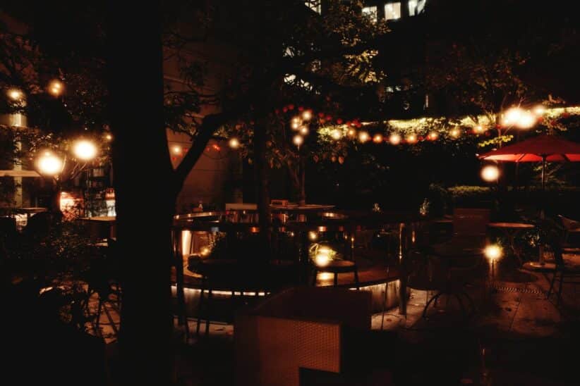 Terrasse nocturne éclairée par des guirlandes lumineuses suspendues entre les arbres