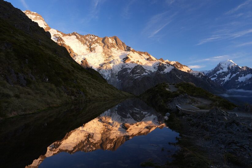 Sommets enneigés éclairés par une lumière rasante et leur reflet dans un lac de montagne resté dans l'ombre